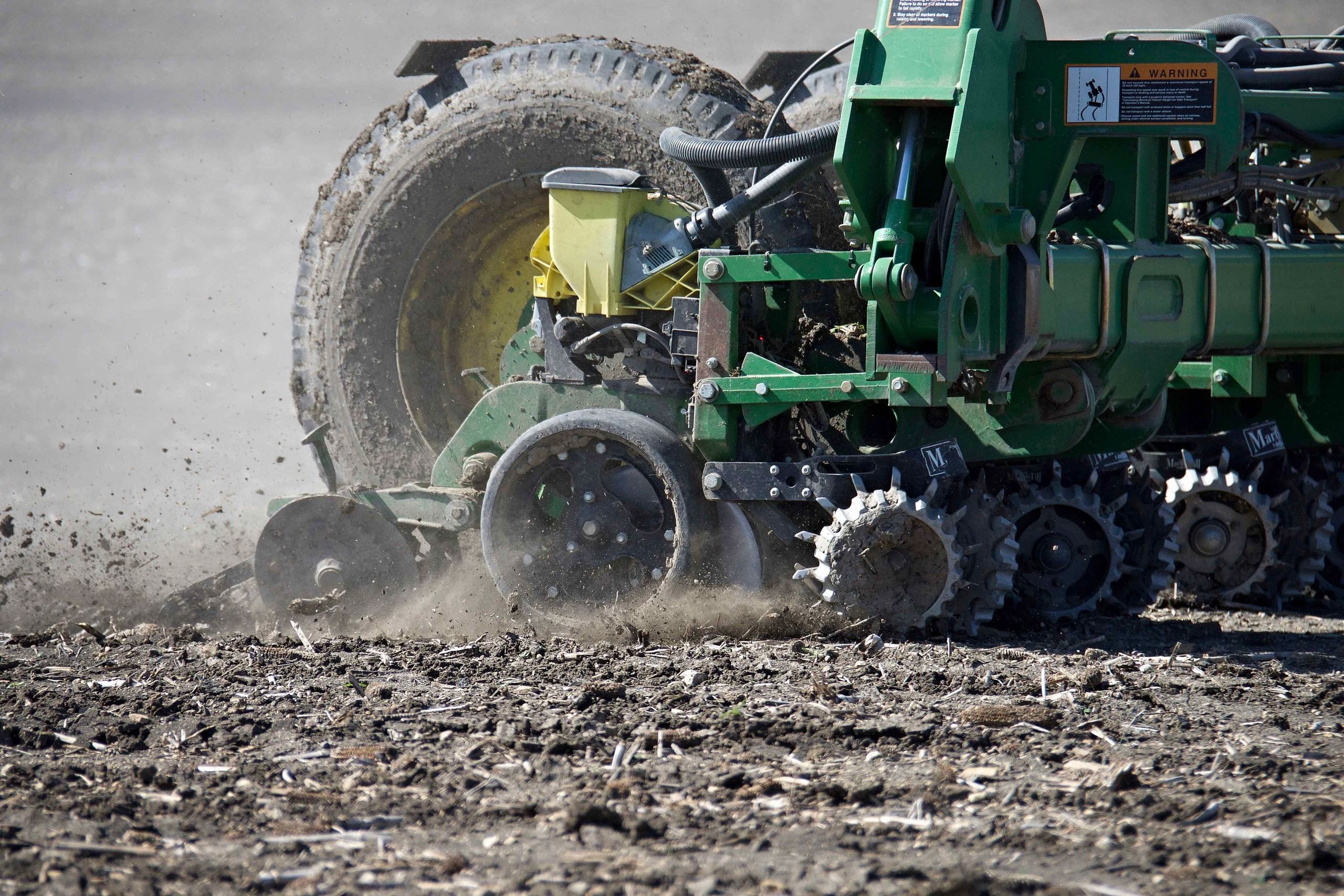 Green farm tractor plowing dusty field